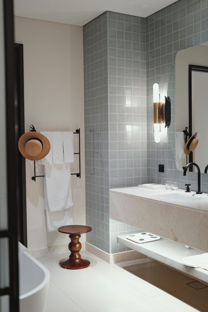 Stylish bathroom with modern fixtures, neutral tones, and elegant decor elements like a straw hat and wooden stool.